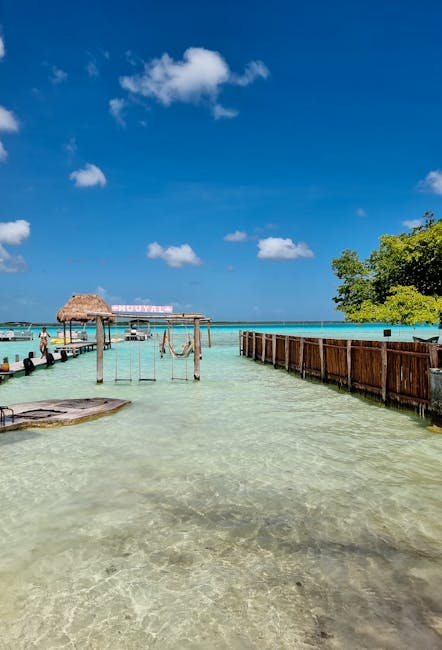 Clear turquoise waters of Bacalar Lagoon with a wooden pier and swings under a bright sky.