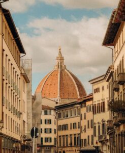 Charming street view of Florence showcasing the famous Duomo dome under a partly cloudy sky.